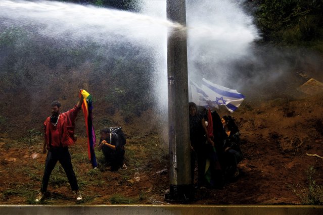 Demonstrators hold flags while being sprayed by a water canyon during a demonstration against Israeli Prime Minister Benjamin Netanyahu and his nationalist coalition government's plan for judicial overhaul, in Tel Aviv, Israel on April 1, 2023. (Photo by Ronen Zvulun/Reuters)