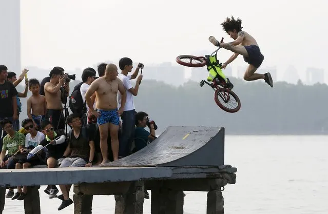 Observers take pictures as an extreme cycling enthusiast (R) performs a stunt with a bicycle before falling into the East Lake in Wuhan, Hubei province, China, July 18, 2015. This activity, requesting participants to ride their bikes and jump into the lake, attracts many extreme cycling enthusiasts from the city, local media reported. (Photo by Reuters/China Daily)