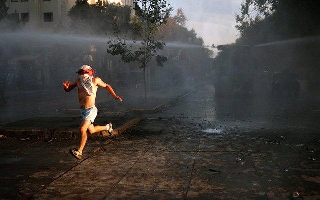 A demonstrator runs away from a vehicle with water cannons during protests against the Government of Sebastian Pinera, at Plaza Italia in Santiago, Chile, 31 October 2019. Ongoing anti-government protests were sparked early in the month after the government announced a price rise in metro tickets. (Photo by Alberto Valdes/EPA/EFE/Rex Features/Shutterstock)