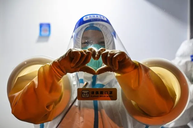 A health worker makes a heart with her hands while waiting to take swab samples from people in the Jing' an district of Shanghai on May 31, 2022, as the city prepares to lift more curbs after two months of heavy-handed restrictions. (Photo by Hector Retamal/AFP Photo)