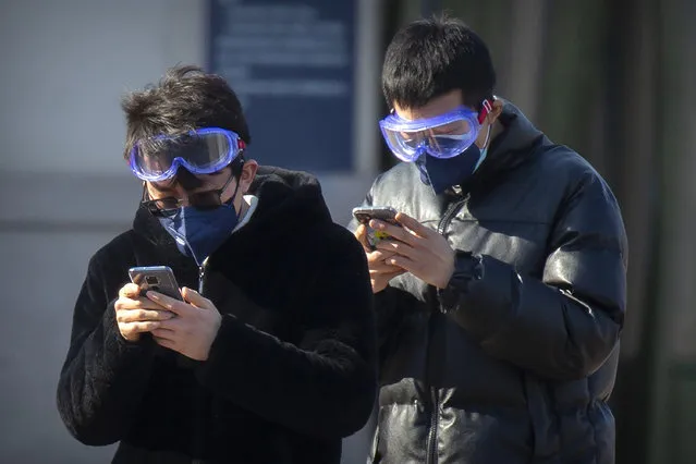Travelers wear face masks and goggles as they use their smartphones outside the Beijing Railway Station in Beijing, Saturday, February 15, 2020. (Photo by Mark Schiefelbein/AP Photo)