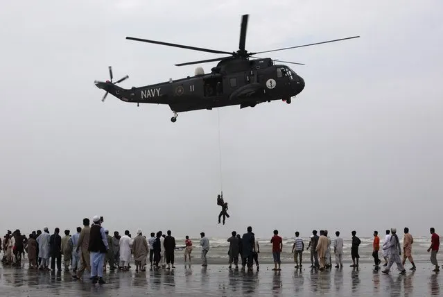People gather as a Pakistan Navy diver attached to a sling rope from a helicopter, holds the body of a man who had drowned on Wednesday, after recovering it from Arabian Sea during a search rescue operation at Karachi's Clifton beach July 31, 2014. At least 19 bodies of victims were recovered after they had drowned while visiting beach as part of Eid al-Fitr celebrations at two different beaches in Karachi on Wednesday, local media reported. (Photo by Akhtar Soomro/Reuters)