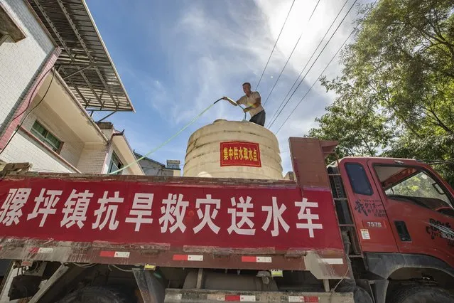 In this photo released by Xinhua News Agency, a worker stands on top of a truck distributing water to residents with a banner which reads “Luoping Drought Relief water truck” in Luoping village of Wushan County in southwestern China's Chongqing, Saturday, August 13, 2022. Unusually high temperatures and a prolonged drought are affecting large swaths of China, affecting crop yields and drinking water supplies for thousands of people. (Photo by Huang Wei/Xinhua via AP Photo)