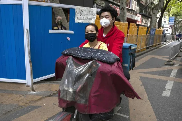 In this Wednesday, April 8, 2020, photo, residents wearing masks to help curb the spread the coronavirus pass by barricades around a community in Wuhan, central China's Hubei province. (Photo by Ng Han Guan/AP Photo)