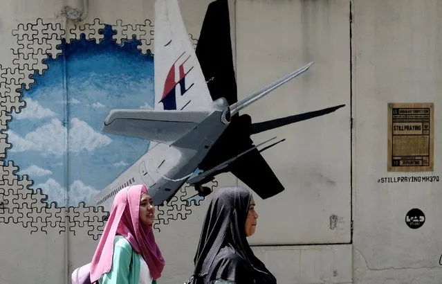 Malaysian women walk in front of a mural of missing Malaysia Airlines MH370 plane in a back-alley in Shah Alam on March 8, 2016. (Photo by Manan Vatsyayana/AFP Photo)