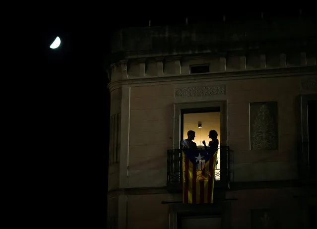 The moon rises next to a couple on a balcony draped with a Catalan separatist flag overlooking Sant Jaume square as people celebrate in front of the Catalan regional government headquarters after the regional parliament declared independence from Spain in Barcelona, Spain, October 27, 2017. (Photo by Jon Nazca/Reuters)
