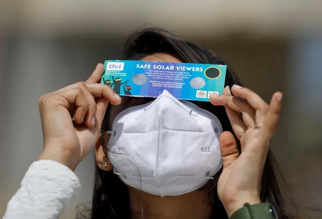 A woman, wearing a protective face mask against the coronavirus disease (COVID-19), uses solar viewers to watch a partial solar eclipse at Gandhinagar, India, June 21, 2020. (Photo by Amit Dave/Reuters)