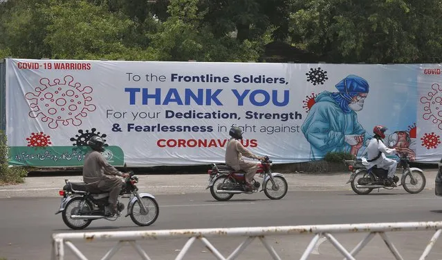 Motorcyclists ride past a banner paying tribute to doctors, nurses, paramedics and other health care providers who are offering care and saving lives during the coronavirus pandemic, hanging along a roadside in Islamabad, Pakistan, Wednesday, July 8, 2020. (Photo by Anjum Naveed/AP Photo)
