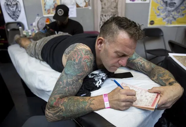 A man attempts to complete a puzzle book as he is tattooed during the International London Tattoo Convention in east London, Britain September 26, 2015. (Photo by Neil Hall/Reuters)