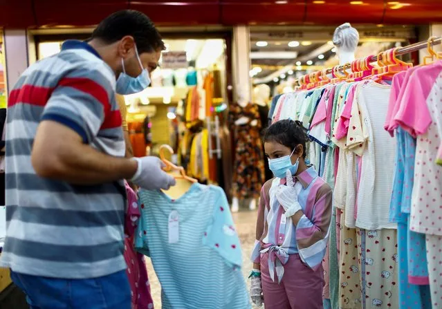 An Iraqi man and a child wear protective face masks while buying clothes at a shop, in preparation for the Muslim festival of Eid al-Adha, as the coronavirus disease (COVID-19) outbreak continues in Baghdad, Iraq, July 29, 2020. (Photo by Thaier Al-Sudani/Reuters)