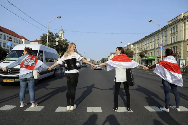 Women cover themselves with old Belarusian national flags as they block a road, during an opposition rally to protest the official presidential election results in Minsk, Belarus, Saturday, September 12, 2020. ( Photo by AP Photo/Stringer)