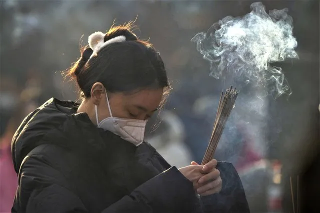 A visitor burns incense as she prays on the first day of the Lunar New Year holiday at the Lama Temple in Beijing, Sunday, January 22, 2023. (Photo by Mark Schiefelbein/AP Photo)