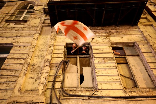 A protester waves a Georgia's national flag from the windows of a building during a demonstration against a draft bill on “foreign influence” in Tbilisi on early April 18, 2024. Thousands protestors rallied in Georgia after lawmakers advanced a controversial “foreign influence” law that opponents say will undermine Tbilisi's longstanding European aspirations. (Photo by Giorgi Arjevanidze/AFP Photo)