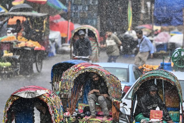 A cyclerickshaw puller takes shelter under the canopy of his vehicle during rainfall in Dhaka on May 14, 2025. (Photo by Munir Uz Zaman/AFP Photo)