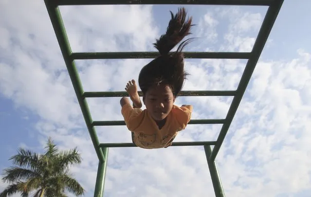 A girl swings upside down on a monkey bar at a playground near the banks of Tonle Sap river in Phnom Penh December 4, 2014. (Photo by Samrang Pring/Reuters)
