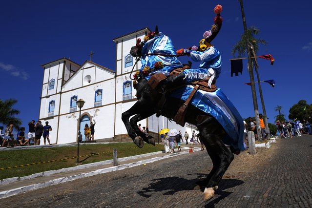 A horseman, wearing a decorative bull mask, and mounted on a prancing horse, attends the Feast of the Divine celebrations, backdropped by the Our Lady of the Rosary Parish, as part of the “Cavalhadas” festival, in Pirenopolis, Goias state, Brazil, Saturday, May 18, 2024. The tradition of the “Cavalhadas” or masked horsemen's festival was brought to Brazil in the 1800s by a Portuguese priest to celebrate the “Holy Spirit” and to commemorate the medieval victory of Iberian Christian knights over the Moors. (Photo by Eraldo Peres/AP Photo)