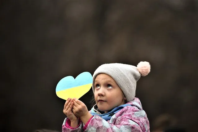 A little girl holds a heart shaped cutout in the colours of the Ukrainian flag, during a protest against Russia's war on Ukraine, marking the first anniversary of Russia's full-scale invasion of Ukraine, in Bucharest, Romania, Friday, February 24, 2023. (Photo by Andreea Alexandru/AP Photo)