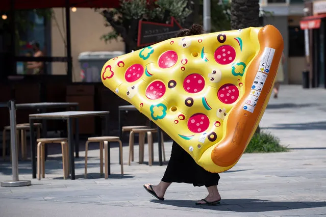 A woman carries an inflatable float with the sahpe of a portion of pizza in a Barcelona, on July 18, 2020. Four million residents of Barcelona have been urged to stay at home as virus cases rise, while EU leaders were set to meet again in Brussels, seeking to rescue Europe's economy from the ravages of the pandemic. (Photo by Josep Lago/AFP Photo)