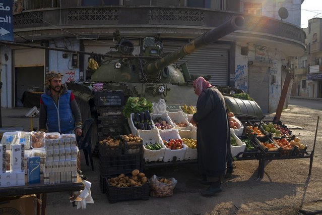 A man looks at fruits and vegetables displayed for sale in front of an ousted Syrian government forces tank that was left on a street in an Alawite neighbourhood, in Homs, Syria, Thursday, December 26, 2024. (Photo by Leo Correa/AP Photo)
