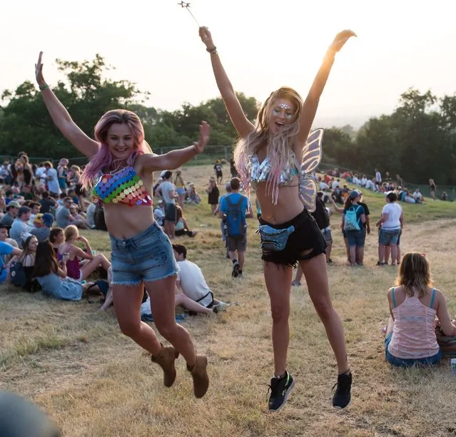 Two pretty female festival goers do a star jump in the evening sun at the Glastonbury Festival, Day 1, United Kingdom on June 21, 2017. The girl on the right is wearing metallic makeup with a matching bikini top, and is carrying a shiny magic wand. (Photo by Richard Isaac/Rex Features/Shutterstock)