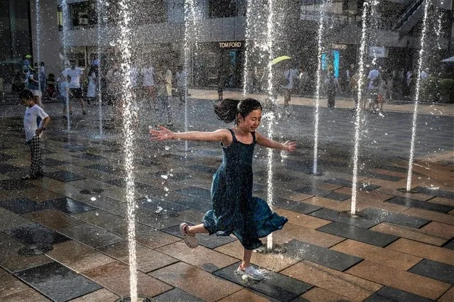 A girl runs through a water fountain at shopping mall to cool off during a heatwave on June 23, 2023 in Beijing. (Photo by Kevin Frayer/Getty Images)