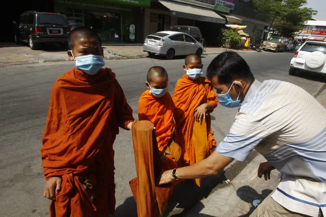 Buddhist monks wearing face masks receive alms from a devotee in Phnom Penh, Cambodia, Wednesday, March 10, 2021. Cambodia on Thursday confirmed its first death from COVID-19 since the pandemic began more than a year ago as it battles a new local outbreak that has infected hundreds of people. (Photo by Heng Sinith/AP Photo)