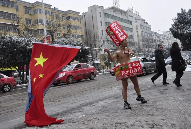 Pedestrians look on as a topless man (C), carrying a Chinese national flag and wearing cardboards printed with advertisements, promotes exercise equipment on a street covered by thin snow in Zhumadian, Henan province January 29, 2015. (Photo by Reuters/Stringer)