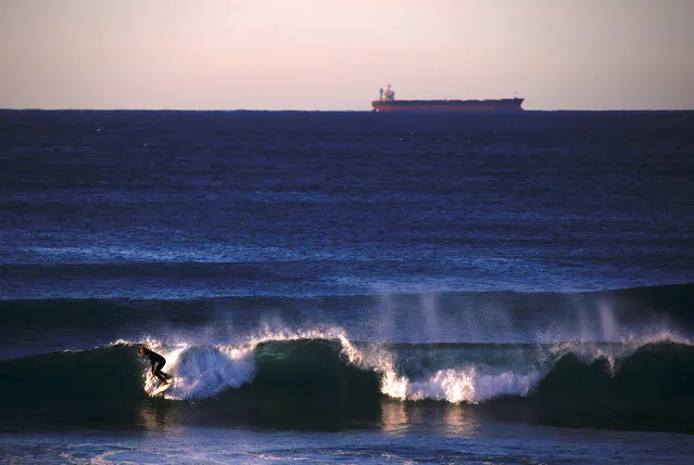 A ship waiting to be filled with a load of coal can be seen behind a surfer riding a wave at Merewether Beach in Newcastle, located north of Sydney in Australia, August 14, 2018. (Photo by David Gray/Reuters)