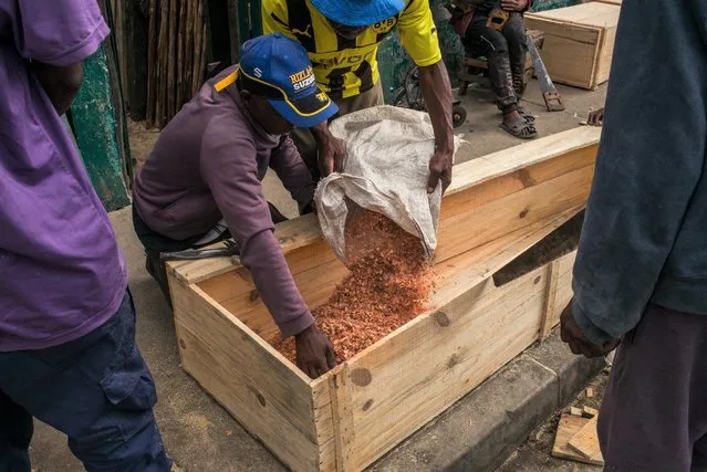 Mr. Jean (C) (not his real name) throws saw dust into a coffin while him and his team of eight carpenters make cheap coffins on the street, even though this activity is prohibited on the public highway, in Antananarivo on April 14, 2021. Since the second wave of the Covid-19 pandemic in Madagascar, which saw the number of deaths increase in the capital, the demand for coffins has also increased considerably. For the past three weeks, Mr. Jean and his team have been producing between 15 and 20 coffins per day, whereas before they were producing only 3 or 4 per day. The coffins, made of pine wood in one hour, are sold between 90,000 and 210,000 Ariary (between 20 and 47 euros). (Photo by RIJASOLO/AFP Photo)