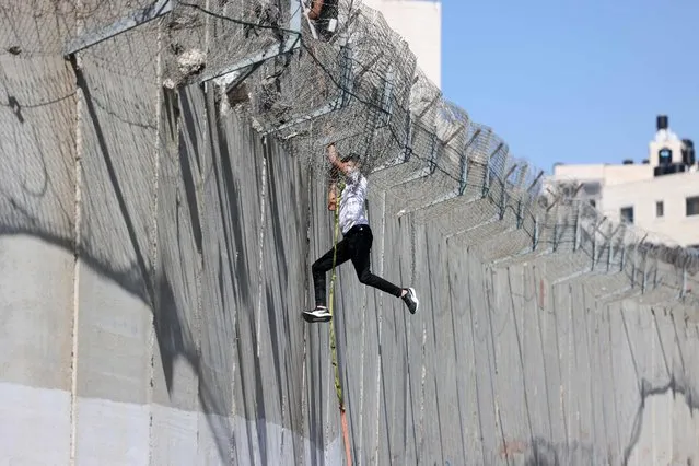 A youth descends on a rope across the concrete wall of Israel's controversial separation barrier into the East Jerusalem neighbourhood of Beit Hanina after having climbed and crossed over from the village of al-Ram, on July 11, 2022. (Photo by Ahmad Gharabli/AFP Photo)