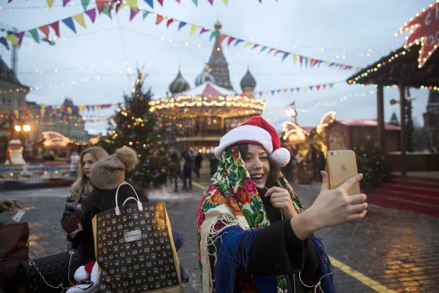A woman dressed in Russian traditional headscarf and Santa Claus hat talks by phone video call at the Christmas Market in Red Square, with St. Basil's Cathedral in the background, in Moscow, Russia, Thursday, December 22, 2016. (Photo by Pavel Golovkin/AP Photo)