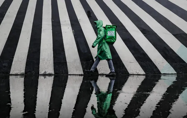 Delivery food man walks on a street during rainfall in front of the graffiti on the wall in Moscow, Russia, 11 August 2021. (Photo by Yuri Kochetkov/EPA/EFE)