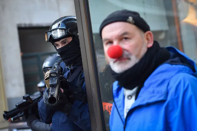A plain-clothes police officer holds his rubber bullets less lethal gun (LBD40) next to a man wearing a red nose during an anti-government demonstration called by the “yellow vests” (gilets jaunes) in Nantes, on February 2, 2019. The “Yellow Vest” (Gilets Jaunes) movement called to pacifically protest against police violence toward participants of the last three months demonstrations in France and for the bam of the use by riot police of both 40-millimetre rubber defencive bullet launcher LBD and GLI-F4 stun grenades, as “Yellow Vest” (Gilets Jaunes) protesters take to the streets for the 12th consecutive Saturday. (Photo by Loïc Venance/AFP Photo)