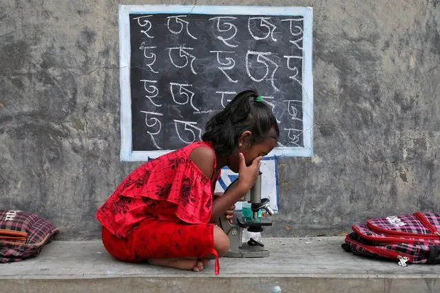 A girl, who does not have access to internet facilities and gadgets, uses a microscope as she attends an open-air class outside a house with its walls converted into black boards following the closure of their schools due to the coronavirus disease (COVID-19) outbreak, at Joba Attpara village in Paschim Bardhaman district in the eastern state of West Bengal, India, September 13, 2021. (Photo by Rupak De Chowdhuri/Reuters)
