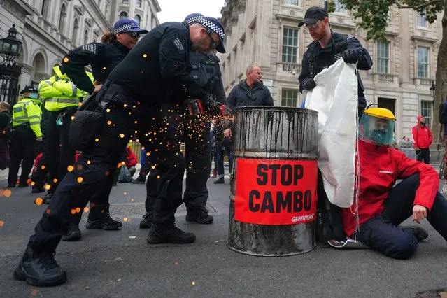 Police officers cutting an oil barrel as campaigners from Greenpeace protest outside Downing Street, London on Monday October 11, 2021, against the Cambo oil field off the west coast of Shetland. (Photo by Victoria Jones/PA Images via Getty Images)
