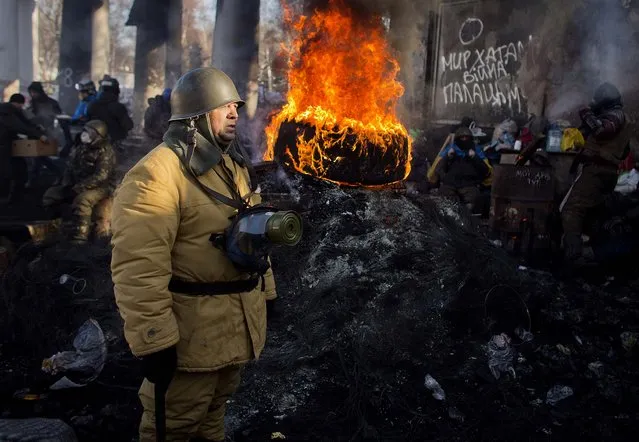 An opposition supporter stands next to a burning tire at a barricade in Kiev, on January 30, 2014. Ukraine's embattled president is taking sick leave, his office announced Thursday, a surprise development that left unclear how efforts to resolve the country's political crisis would move forward. Protesters have been calling for his resignation for two months. The sign at right reads: “Peace to the Villages, War to the Palaces”. (Photo by Darko Bandic/Associated Press)