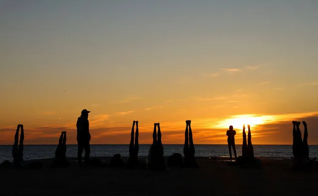 People perform yoga on the breakwater of the Barceloneta beach during the sunrise in Barcelona, Spain on January 18, 2024. (Photo by Nacho Doce/Reuters)