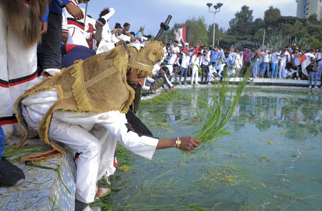 Oromos throw grass and flowers into a pool of water as they celebrate the annual Irreecha festival in the capital Addis Ababa, Ethiopia, Saturday, October 2, 2021. Ethiopia's largest ethnic group, the Oromo, on Saturday celebrated the annual Thanksgiving festival of Irreecha, marking the end of winter where people thank God for the blessings of the past year and wish prosperity for the coming year. (Photo by AP Photo/Stringer)