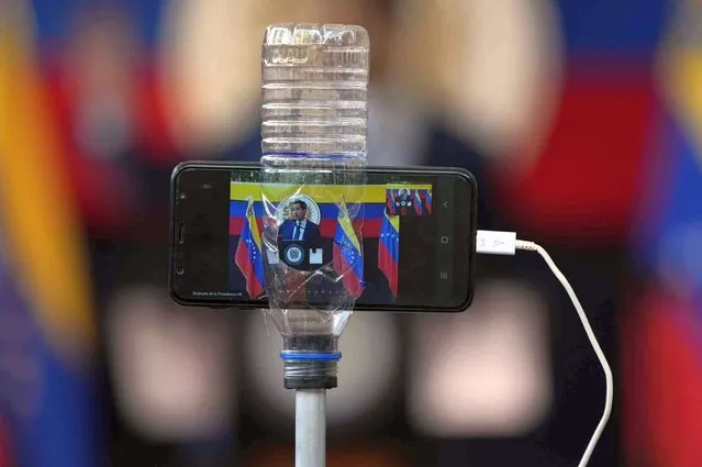 Opposition leader Juan Guaido is seen on the screen of a cell phone inside a plastic bottle hold it steady as he speaks to the press in Caracas, Venezuela, Monday, November 22, 2021, the day after regional elections. Under the scrutiny of international observers, Venezuelans cast ballots for thousands of local races in elections that for the first time in four years included major opposition participation. (Photo by Ariana Cubillos/AP Photo)