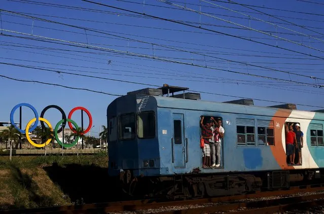 Passengers hang on the doors of a train as it passes the Olympic rings placed at the Madureira Park ahead the Rio 2016 Olympic Games, in Rio de Janeiro May 22, 2015. The rings, the official symbol of the Olympic Games, was donated to Rio by Britain after they decorated the Tyne Bridge in Newcastle during the 2012 London Olympic Games. (Photo by Ricardo Moraes/Reuters)