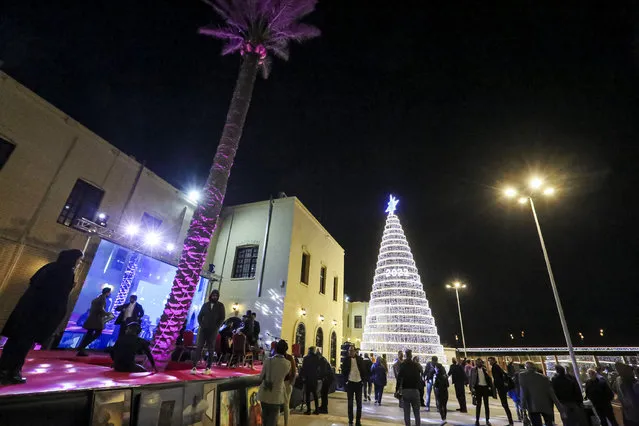 People walk past an installation depicting a Christmas tree made of lights and marking the new year 2022 during the reopening of the renovated al-Mutanabbi street, the historic heart of the book trade and an outlet for writers and intellectuals, in the centre of Iraq's capital Baghdad on December 25, 2021. (Photo by Sabah Arar/AFP Photo)