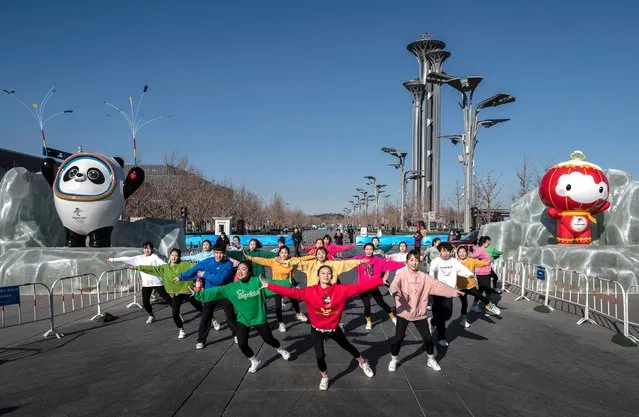 A group dances as they are filmed in front of Beijing 2022 Winter Olympics mascots Bing Dwen Dwen, left, and Shuey Rhon Rhon near the Olympic Tower, background, next to the National Stadium on January 13, 2022 in Beijing, China. The area is home to a number of Olympic venues including the National Stadium, also known as the Bird's Nest, where the opening ceremonies will be held when the Games open on February 4th. (Photo by Kevin Frayer/Getty Images)