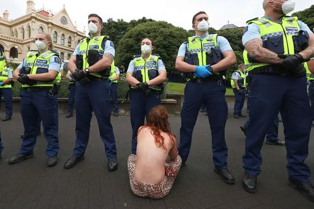 A woman sits in front of police before they moved in to evict protesters in the parliament grounds in Wellington on February 10, 2022, on the third day of demonstrations against Covid-19 restrictions, inspired by a similar demonstration in Canada. (Photo by Marty Melville/AFP Photo)