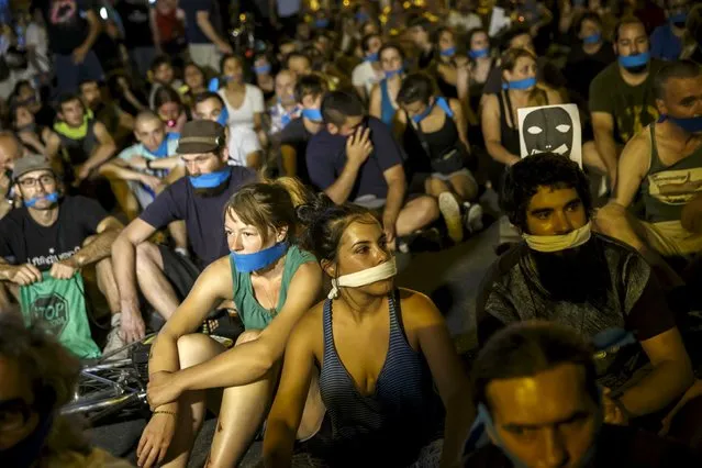 Demonstrators with their mouths taped sit outside the Spanish parliament during a protest against Spanish government's new security law in central Madrid, Spain, early July 1, 2015. Spanish government's new security law, which toughens fines for unauthorised street protests, comes into effect July 1. Critics consider it a violation of the right to protest and a limit to free expression and have labelled it “Ley Mordaza” (Gag Law). (Photo by Juan Medina/Reuters)