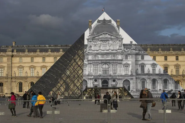 People walk in front of the Louvre Pyramid covered with a giant photograph of the museum by French artist and photographer JR, on May 19, 2016 in Paris. Invited by the Louvre, the artist intends to tranform one of the Louvre's symbols, the Pyramid, “with a surprising anamorphic image”, according to the museum. The exhibition “Contemporary art – JR at the Louvre” will run from May 25 to June 27, 2016. (Photo by Joel Saget/AFP Photo)