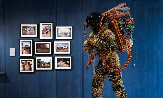 Refugee Astronaut III by Yinka Shonibare stands next to a series of photographs by Adam Chodzko at Wellcome Collection in London, England on September 03, 2019. This lifesize figure wears a suit made from a fabric reminiscent of traditional Nigerian textiles. Carrying a net of possessions, Shonibare’s work invites visitors to create their own stories about who the figure might be, where they have come from and why they had to leave Earth in such a hurry. (Photo by Steven Pocock/Wellcome Collection)