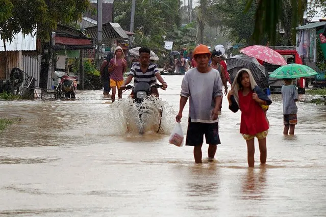 Residents and a motorist wade through a flooded street after heavy rains brought about by Tropical storm Agaton in Abuyog town, Leyte province, southern Philippines on April 11, 2022. (Photo by Bobbie Alota/AFP Photo)