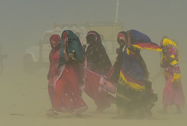 People walk through a sand storm at the Sangam, the confluence of the rivers Ganges, Yamuna and mythical Saraswati in Allahabad on April 19, 2022. (Photo by Sanjay Kanojia/AFP Photo)