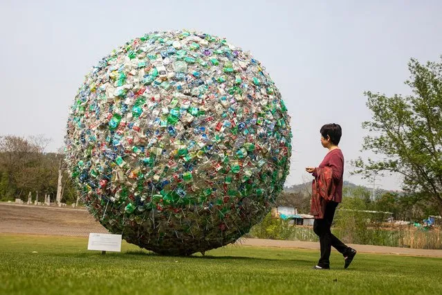 People pass an art installation titled Common Home by Pingwei Ge on April 2, 2022 in Wuhan, Hubei province, China. The meaning of this artistic decoration takes the earth, our common home as its from element, The artist binds the abandoned plastic bottles with locking ties to form the image of “plastic bacteria” which represents the potential ecological hazards and visual pollution caused by the hard to degrade plastic waste. (Photo by Getty Images)