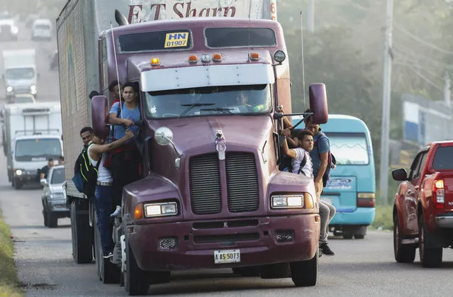 Migrants ride on the side of a truck moving along the highway, in hopes of reaching the distant United States, in San Pedro Sula, Honduras, early Wednesday, January 15, 2020. Hundreds of Honduran migrants started walking and hitching rides Wednesday from the city of San Pedro Sula, in a bid to form the kind of migrant caravan that reached the U.S. border in 2018. (Photo by Delmer Martinez/AP Photo)